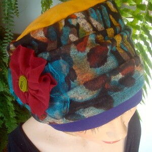 May include: A colorful patterned fabric hat with a red flower accent. The hat has a blue and yellow trim.