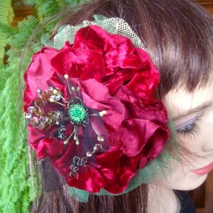 Puede incluir: Una pinza para el pelo de terciopelo rojo con adornos verdes y dorados. La flor est&aacute; en capas y tiene una base de tul.