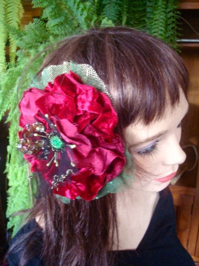 Puede incluir: Una pinza para el pelo de terciopelo rojo con una red verde y adornos dorados y negros. La pinza se lleva en el pelo casta&ntilde;o de una mujer.