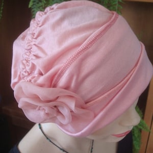 May include: A pink satin turban with a large pink flower accent. The turban is made of a soft, stretchy fabric and has a gathered design.
