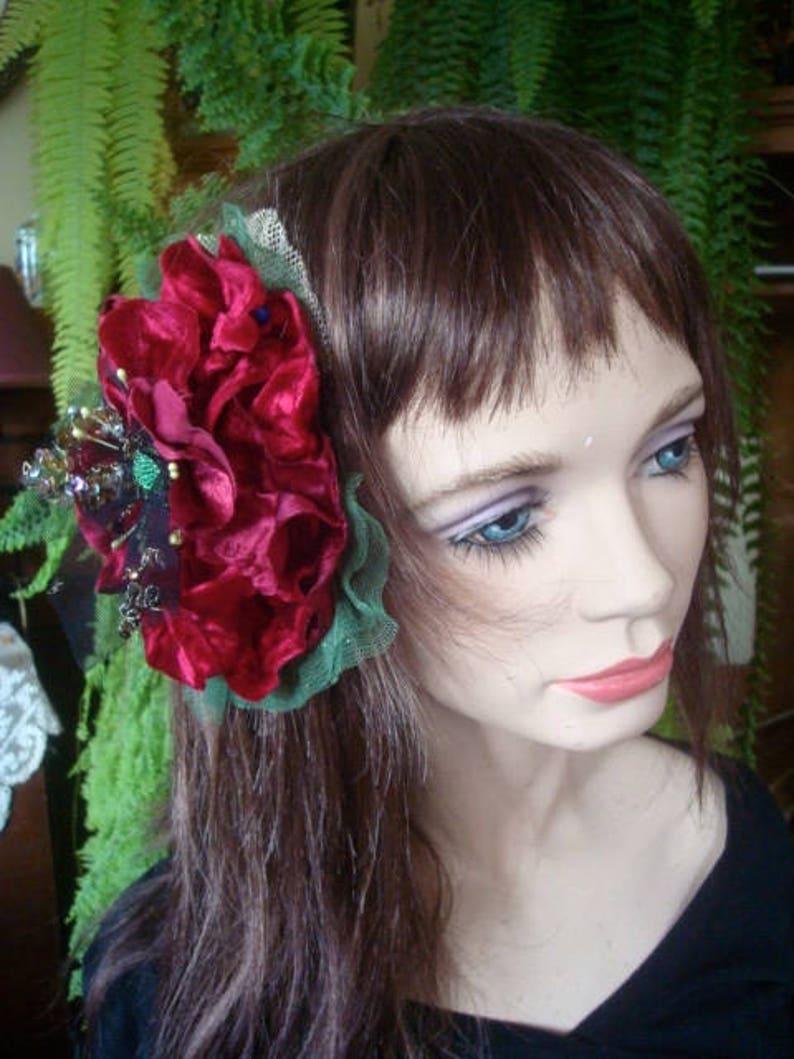 Puede incluir: Una pinza para el pelo de terciopelo rojo con hojas verdes y un adorno de cuentas plateadas y negras. La pinza se lleva en el pelo casta&ntilde;o de una mujer.