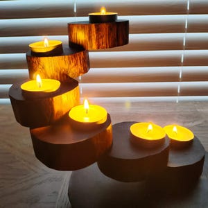 May include: A wooden candle holder with a cascading design, featuring five lit tea lights. The holder is made of natural wood with a dark brown finish.