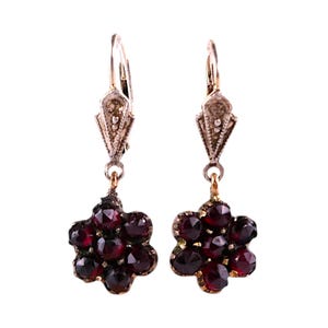 May include: A pair of antique earrings featuring a cluster of deep red gemstones in a floral design. The earrings have a silver-tone top with a decorative element and a gold-tone setting for the gemstones. The gemstones are faceted and catch the light.