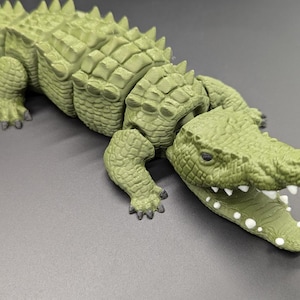 Op de afbeelding: Een groen plastic speelgoedkrokodil met een getextureerd, schubbig lichaam en een open mond die witte tanden laat zien.
