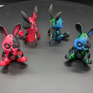 May include: Four 3D printed rabbit keyrings. Two are red and black, and two are blue and green. Each rabbit has a different design on its face.