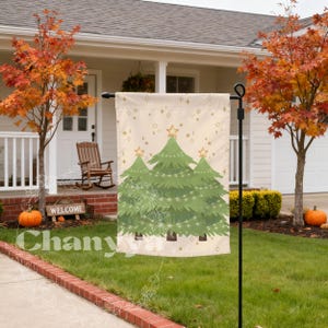 May include: A beige Christmas garden flag featuring three green Christmas trees with star toppers and string lights. The flag has a pattern of gold stars and is displayed outdoors in front of a house.