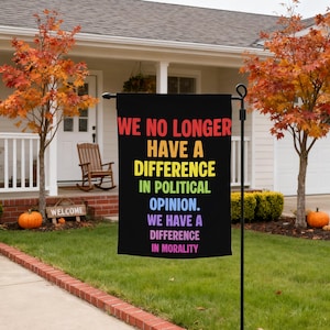 May include: A rectangular black garden flag featuring multi-colored text that reads: WE NO LONGER HAVE A DIFFERENCE IN POLITICAL OPINION. WE HAVE A DIFFERENCE IN MORALITY. The flag is mounted on a black metal stand positioned in a grassy yard.