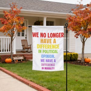 May include: A white garden flag featuring rainbow-coloured text that reads: WE NO LONGER HAVE A DIFFERENCE IN POLITICAL OPINION. WE HAVE A DIFFERENCE IN MORALITY. The flag is mounted on a black metal stand positioned in a grassy front garden.