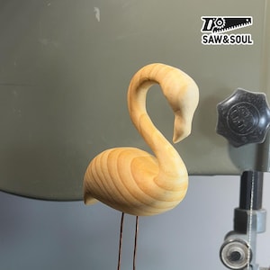 Puede incluir: Escultura de flamenco de madera clara, con cuello curvado y detalles de plumas. Se apoya sobre finas patas metálicas. El logotipo "SAW&SOUL" es visible en la esquina superior derecha.