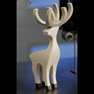 May include: A light-colored wooden deer figurine with prominent antlers and dark-toned hooves. The sculpture features smooth, curved lines and a natural wood grain finish. The logo SAW&SOUL is visible in the upper left corner of the image.