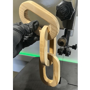 Può includere: Una catena di legno composta da più anelli ovali che si incastrano. La catena è in fase di taglio su una sega a nastro.