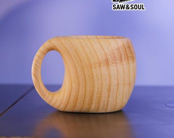 May include: A handcrafted wooden mug with a large, rounded handle. The mug is made from light-colored wood, showcasing the natural grain. The text "SAW&SOUL" is printed on a white sticker in the upper right corner.
