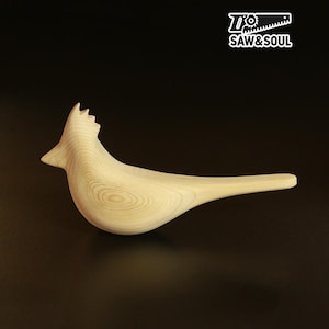 May include: A wooden bird sculpture with a light wood grain finish. The bird has a long tail and a detailed head with a crest. The logo "Saw & Soul" is in the upper right corner.