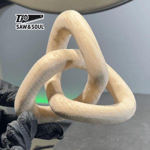 May include: A wooden knot sculpture in the shape of a triangle. The sculpture is made of light brown wood and has a smooth, polished finish.