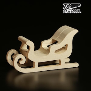 Może przedstawiać: Małe, niewykończone drewniane sanie z zakrzywionymi płozami i siedziskiem. Sanie wykonane są z jasnego drewna i mają klasyczny design. Logo "Saw & Soul" znajduje się w prawym górnym rogu.