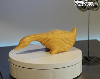 May include: A handcrafted wooden sculpture of a stylized bird or animal, with a smooth, light-colored finish. The sculpture is displayed on a white rotating platform. The logo "SAW&SOUL" is visible in the upper right corner.