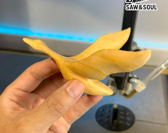 May include: A wooden sculpture of a flying goose, crafted from light-colored wood. The bird is depicted mid-flight with outstretched wings and a long neck. The logo "SAW&SOUL" is visible in the background.