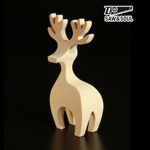 May include: A wooden reindeer figurine with a minimalist design. The light-coloured wood is unpainted, showcasing the natural grain. The antlers are detailed, and the body has a curved silhouette. The logo "Saw & Soul" is in the upper right corner.