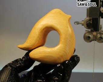 May include: A light-colored, wooden bird-shaped object with a large hole in the center. The object is held in a black gloved hand. The logo "SAW & SOUL" is in the upper right corner.