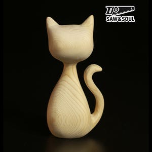 Peut inclure: Figurine de chat en bois clair, avec une finition lisse et naturelle. Le chat est représenté dans une pose stylisée, avec une queue recourbée et des oreilles pointues. Le logo "SAW & SOUL" est visible. La figurine mesure environ 20 cm de haut.