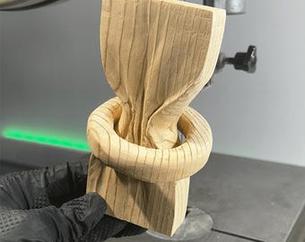 May include: A wooden sculpture of a knot, with a smooth, light brown finish. The knot is carved with intricate details and appears to be made from a single piece of wood.
