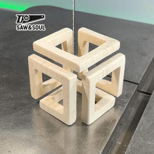 May include: A wooden cube with four interlocking squares, each with a square opening. The cube is made of light-coloured wood and is being cut by a saw.