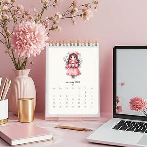May include: A desk calendar for January 2026 featuring a watercolor illustration of a girl in a pink coat and hat. The calendar is on a pink desk with a laptop, flowers in a vase, a gold cup, and a notebook.