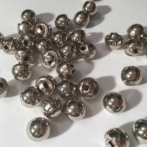 Op de afbeelding: Een grote groep ronde zilveren metalen knopen met een klein gaatje in het midden van elke knop.