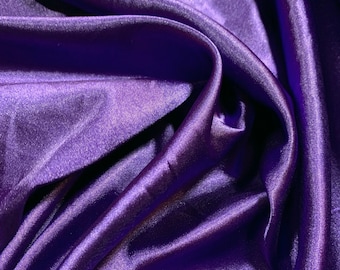 May include: A close-up of a smooth, silky fabric in a deep purple hue. The fabric is draped and folded, creating soft, flowing lines and a luxurious feel.