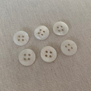 May include: Six white round buttons with four holes each. The buttons are made of a pearlescent material.