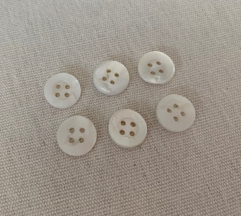 May include: Six white round buttons with four holes each. The buttons are made of a pearlescent material.