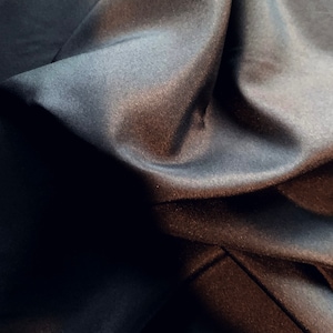 May include: Close-up of a dark gray fabric with a smooth, silky texture. The fabric is draped and folded, creating soft, flowing lines.