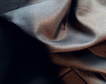 May include: Close-up of a dark gray fabric with a smooth, silky texture. The fabric is draped and folded, creating soft, flowing lines.