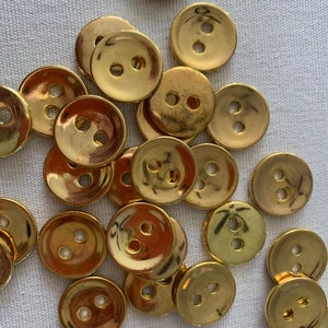 Peut inclure: Un tas de boutons de couleur or avec deux trous chacun. Les boutons sont ronds et ont un centre légèrement surélevé.