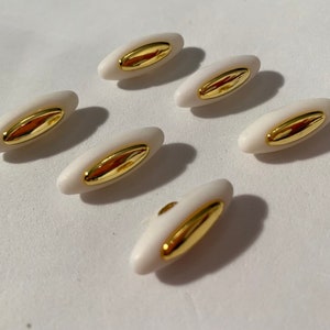 May include: Six white oval buttons with a gold center. The buttons have a smooth, glossy finish.