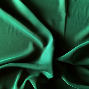 May include: A close-up of a deep green fabric with a smooth, silky texture. The fabric is draped and folded, creating soft, flowing lines.