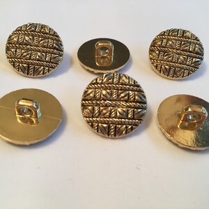 May include: Six gold-colored buttons with a woven pattern. The buttons have a shank on the back.