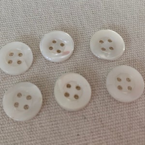 May include: Six white pearl buttons with four holes each. The buttons are arranged in two rows of three.