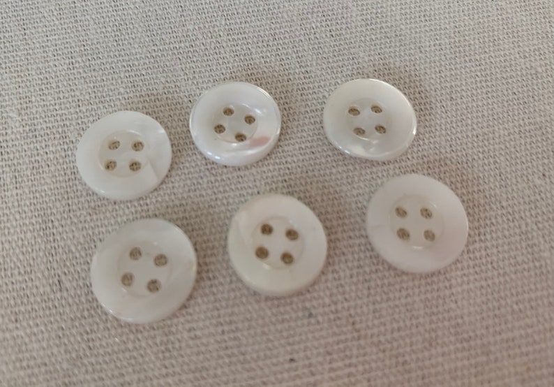 May include: Six white pearl buttons with four holes each. The buttons are arranged in two rows of three.