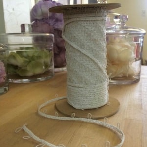 Op de afbeelding: Een spoel met witte gecrochete bies met een bruine kartonnen spoel. De bies heeft kleine lussen langs de rand.