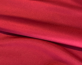 May include: A close-up of a smooth, deep red fabric with a subtle sheen. The fabric is folded in a way that creates a soft, flowing drape.