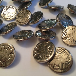 May include: A collection of silver-toned buttons with a raised design of a person's face. The buttons are round and have a smooth, shiny finish.
