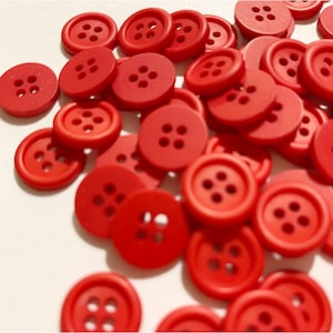 May include: A large pile of red plastic buttons with four holes each. The buttons are scattered on a white surface.