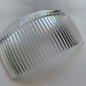May include: A clear plastic comb with a curved shape and fine teeth.