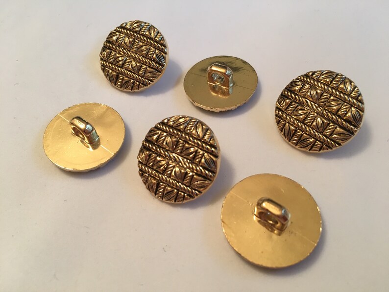 May include: Five gold-colored buttons with a raised, woven design. The buttons have a shank on the back.