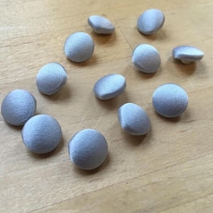 Può includere: Una collezione di dodici bottoni rotondi di colore azzurro chiaro. I bottoni sono fatti di un tessuto morbido e liscio.