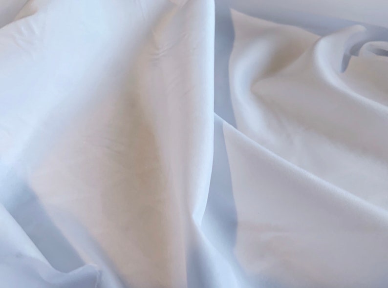 May include: White fabric with soft folds and wrinkles. The fabric is smooth and silky.
