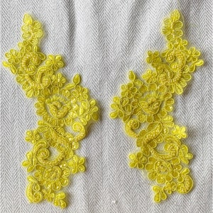 May include: Two yellow floral lace appliques with a beaded design on a white background.