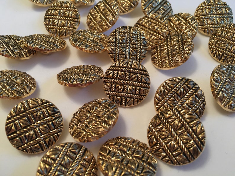 May include: A collection of gold-toned buttons with a woven pattern. The buttons are round and have a raised design.