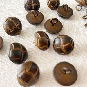 May include: A collection of brown leather buttons with a woven design. Each button has a small loop on the back for sewing.